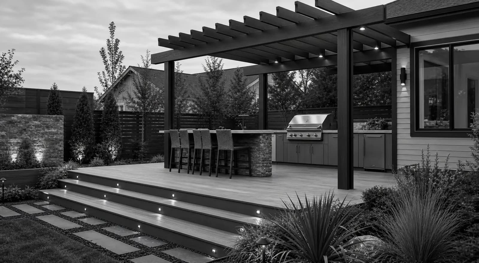 Finished outdoor kitchen, pergola, and deck in a landscaped residential backyard.